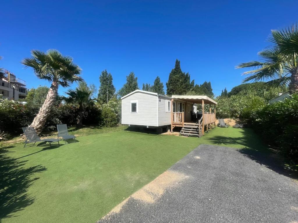 une petite cabine blanche sur une pelouse avec un palmier dans l'établissement Mobi Home Palmiers 2, à Valras-Plage