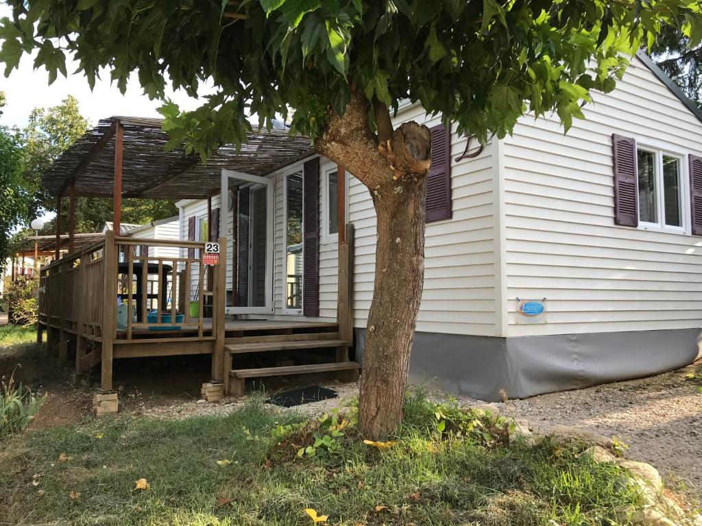 une maison blanche avec une véranda et un arbre dans l'établissement CAMPING GINASSERVIS Mobile-home Flores, à Ginasservis 5 autres photos