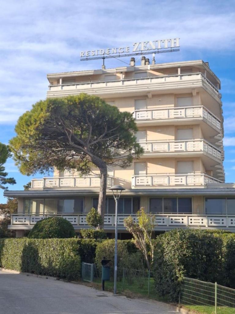 un grand bâtiment avec un arbre devant dans l'établissement Residence Zenith, à Caorle