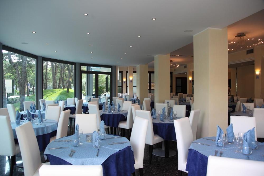 une salle à manger avec des tables bleues et des chaises blanches dans l'établissement Hotel Bellevue, à Lignano Sabbiadoro