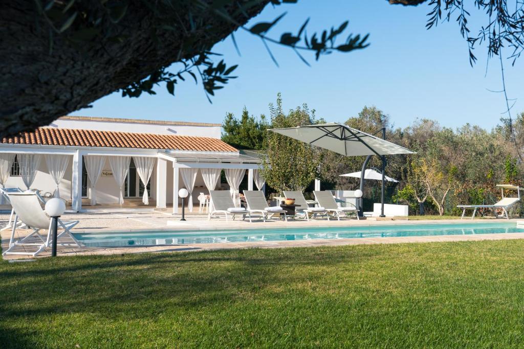 une maison avec une piscine, des chaises et un parasol dans l'établissement Villa L'Ulivo by Bianco Puglia Vacanze, à San Vito dei Normanni