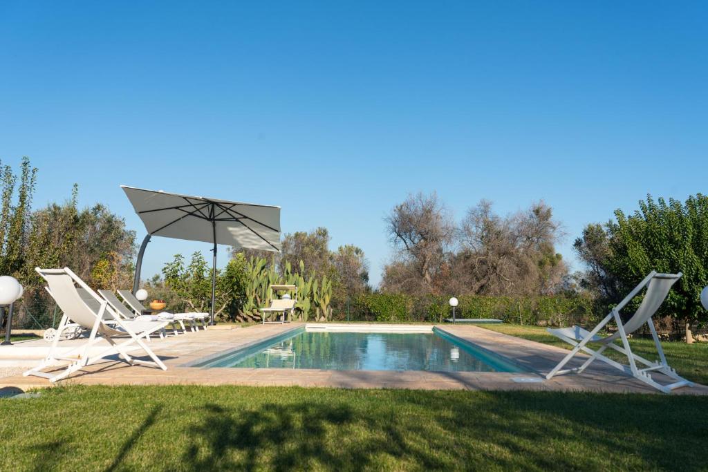 - une piscine avec 2 chaises, une table et un parasol dans l'établissement Villa L'Ulivo by Bianco Puglia Vacanze, à San Vito dei Normanni