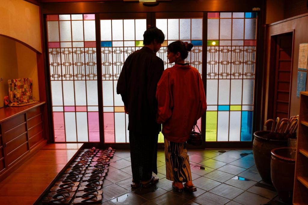 un homme et une femme debout devant une porte en verre teinté dans l'établissement Kinosaki Onsen Hanakouji Saigetsu, à Toyooka