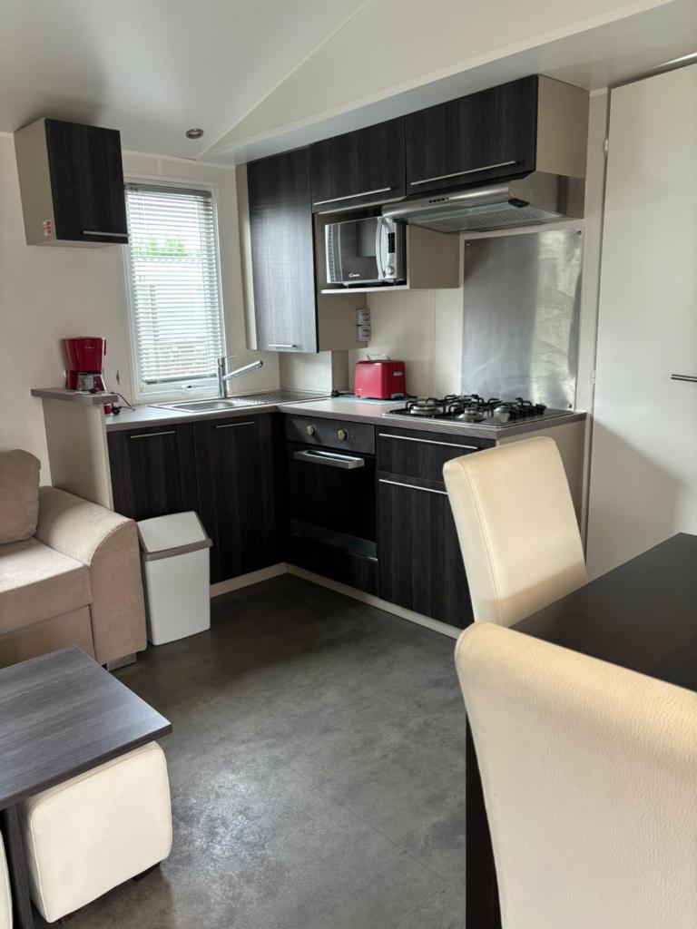 une cuisine avec des armoires noires, une table et des chaises dans l'établissement Mobil home 6 personnes, à Argelès-sur-Mer