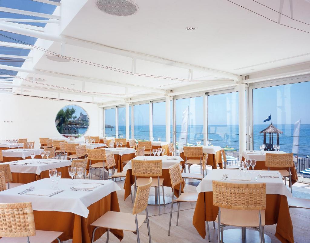 un restaurant avec des tables et des chaises blanches et des fenêtres dans l'établissement Hotel Amyclae, à Sperlonga
