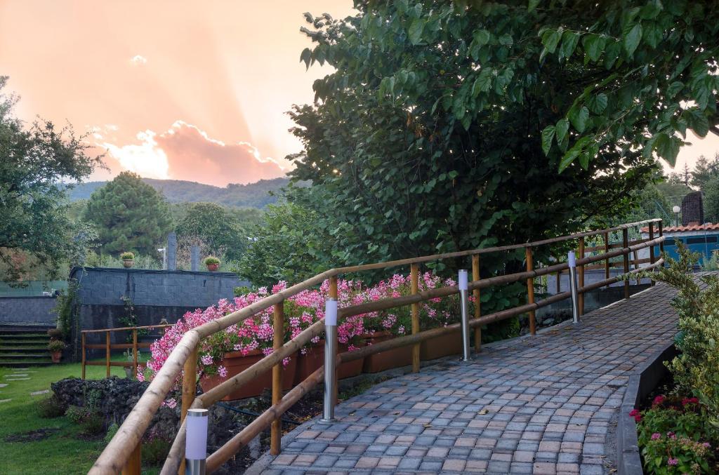 une passerelle en bois avec des fleurs roses dans un jardin dans l'établissement Villa del Gelso - Chalet nel Parco dell'Etna, à Mascali