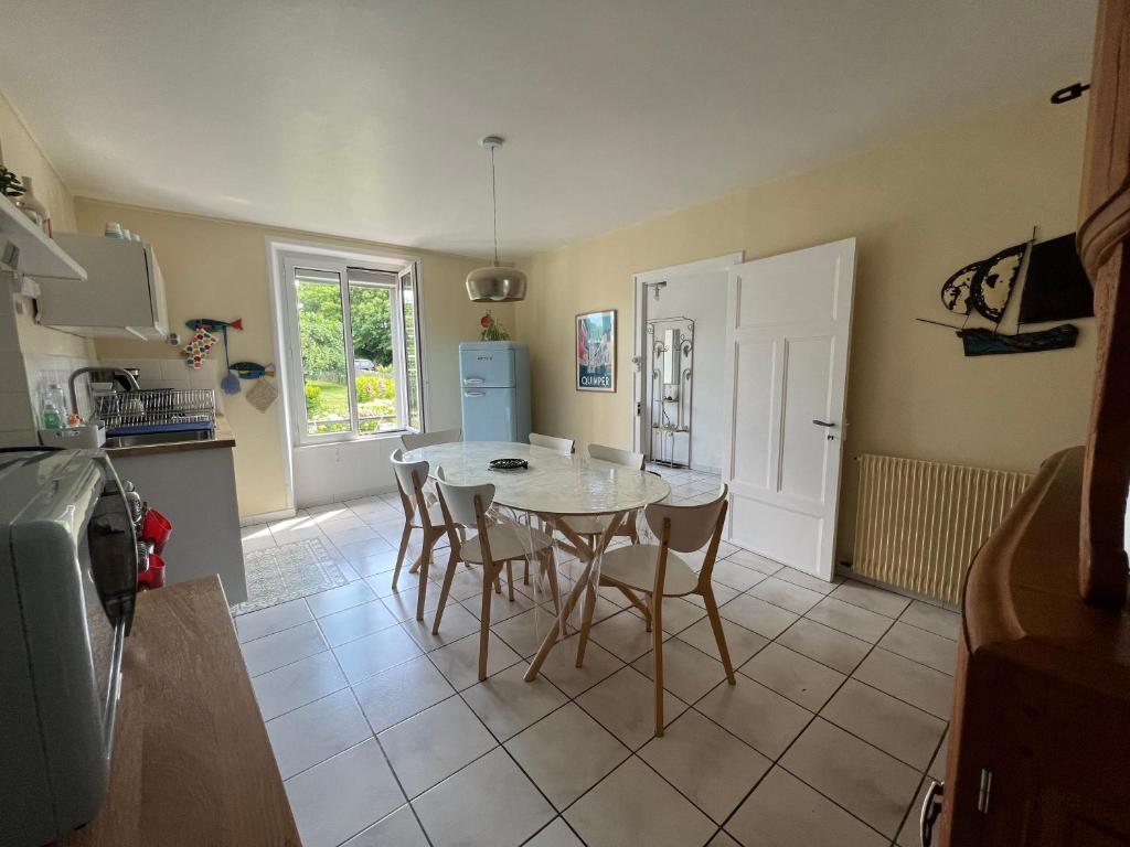 une cuisine avec une table, des chaises et un réfrigérateur dans l'établissement Maisons Les Gites de l'Odet, à Clohars-Fouesnant