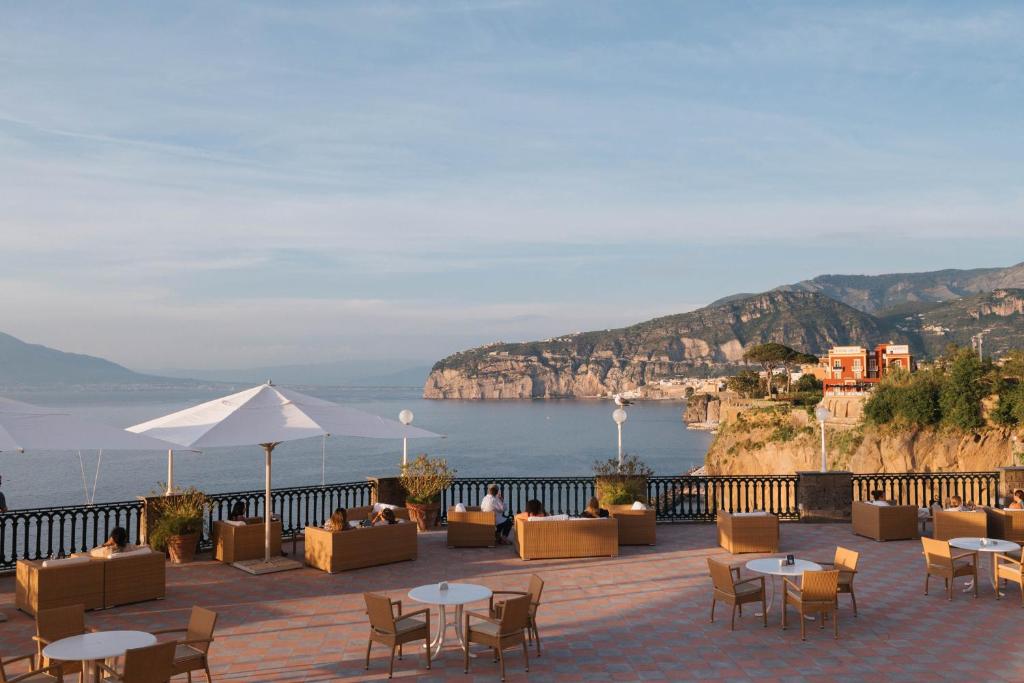 un patio avec tables et chaises et vue sur l'océan dans l'établissement Grand Hotel Europa Palace Sorrento, à Sorrente