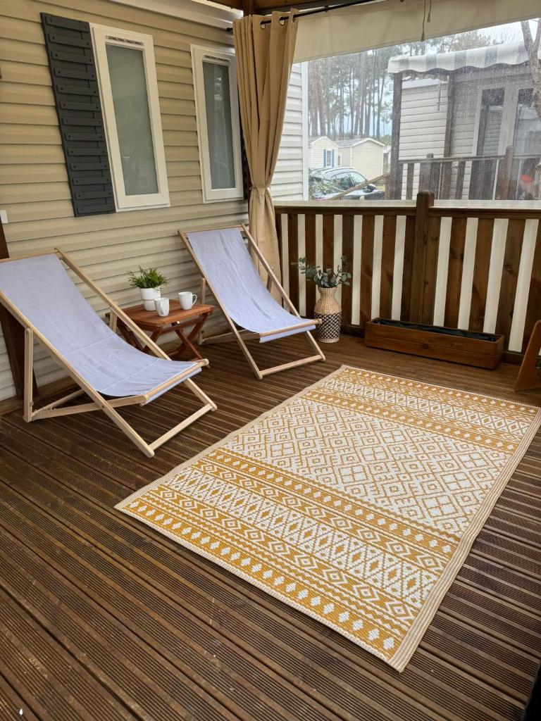 - une terrasse couverte avec 2 chaises, une table et un tapis dans l'établissement Mobil Home MarieVa "Les dunes de Contis", à Saint-Julien-en-Born
