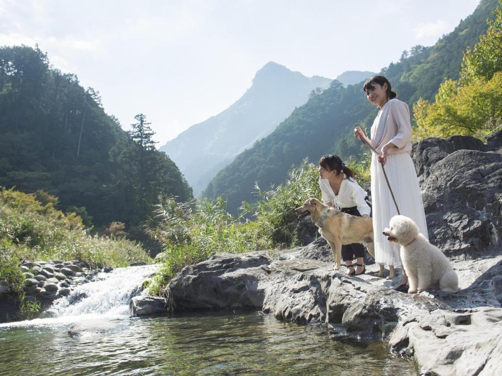 deux femmes et un chien debout sur des rochers près d'une rivière dans l'établissement Matsusaka Doggie Paradise Hotel Smeall, à Matsuzaka