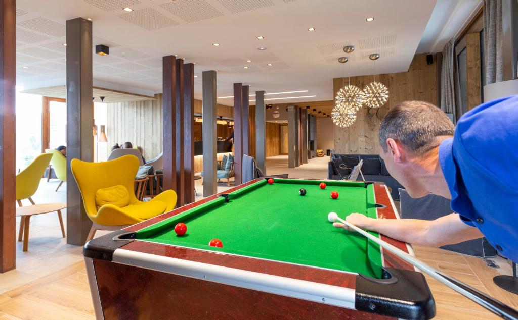 un homme jouant au billard dans une salle avec un billard dans l'établissement Résidence Club MMV Les Chalets des Cimes, aux Saisies