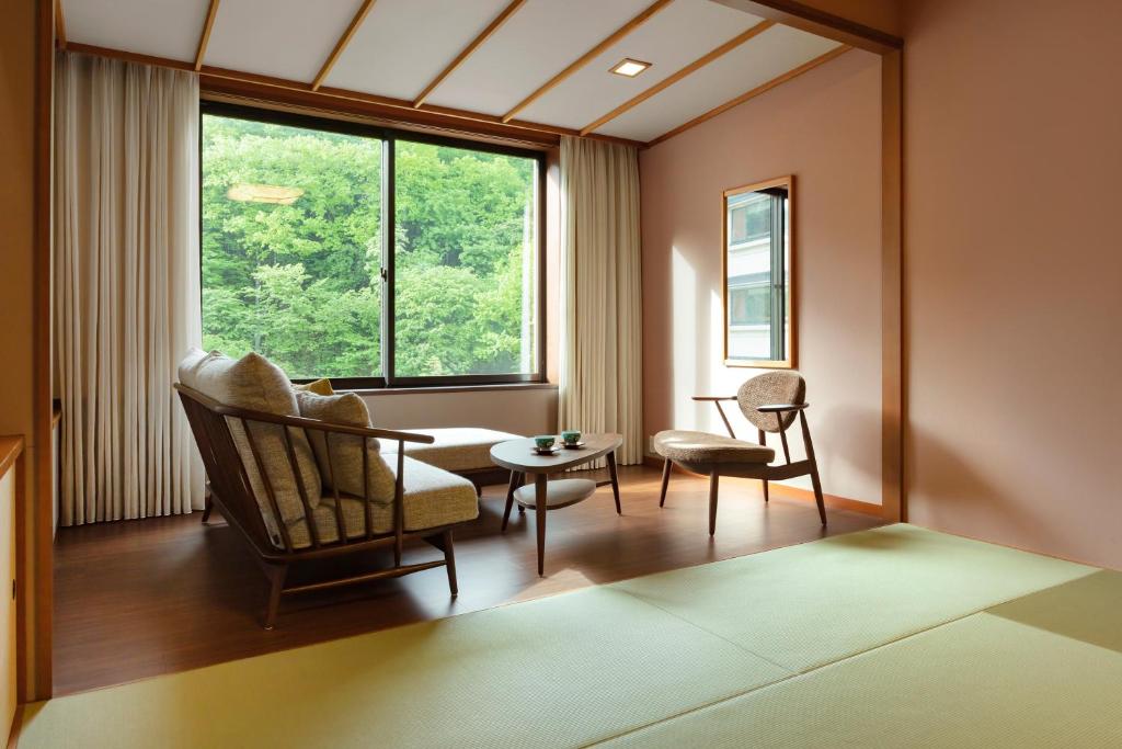 une pièce avec une chaise, une table et une fenêtre dans l'établissement Dai-ichi Takimotokan, à Noboribetsu