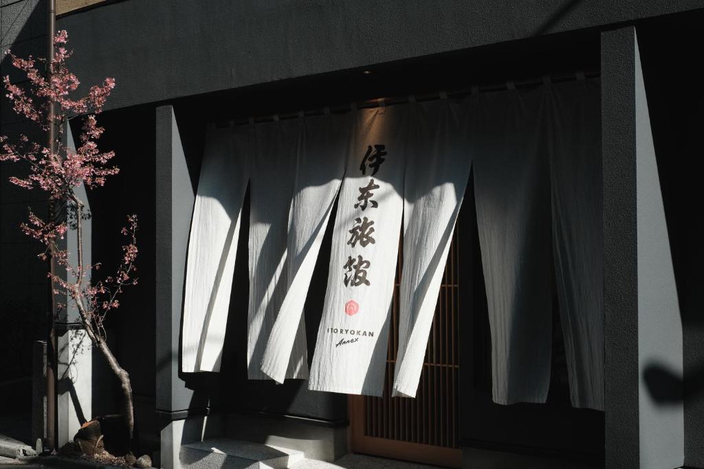 une porte avec des rideaux blancs et un panneau sur celle-ci dans l'établissement Ito Ryokan, à Tokyo