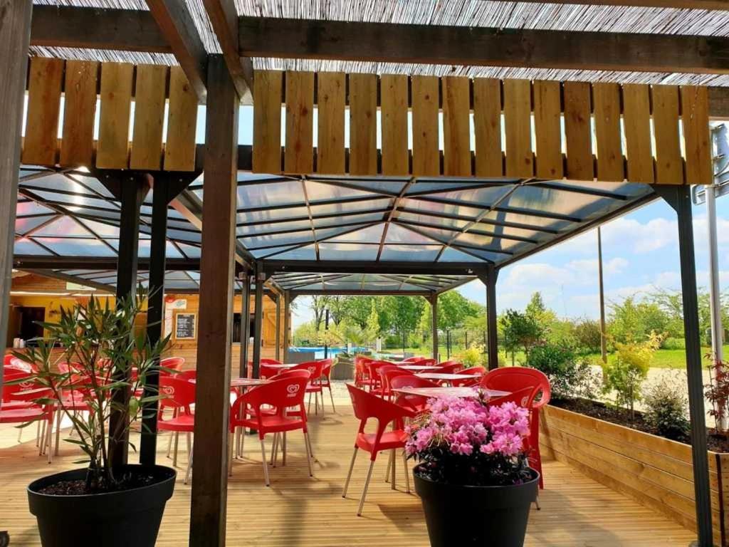 un patio avec des chaises rouges et des tables sous une pergola dans l'établissement Camping 3 étoiles - Piscine - ccbaice, à Loudéac