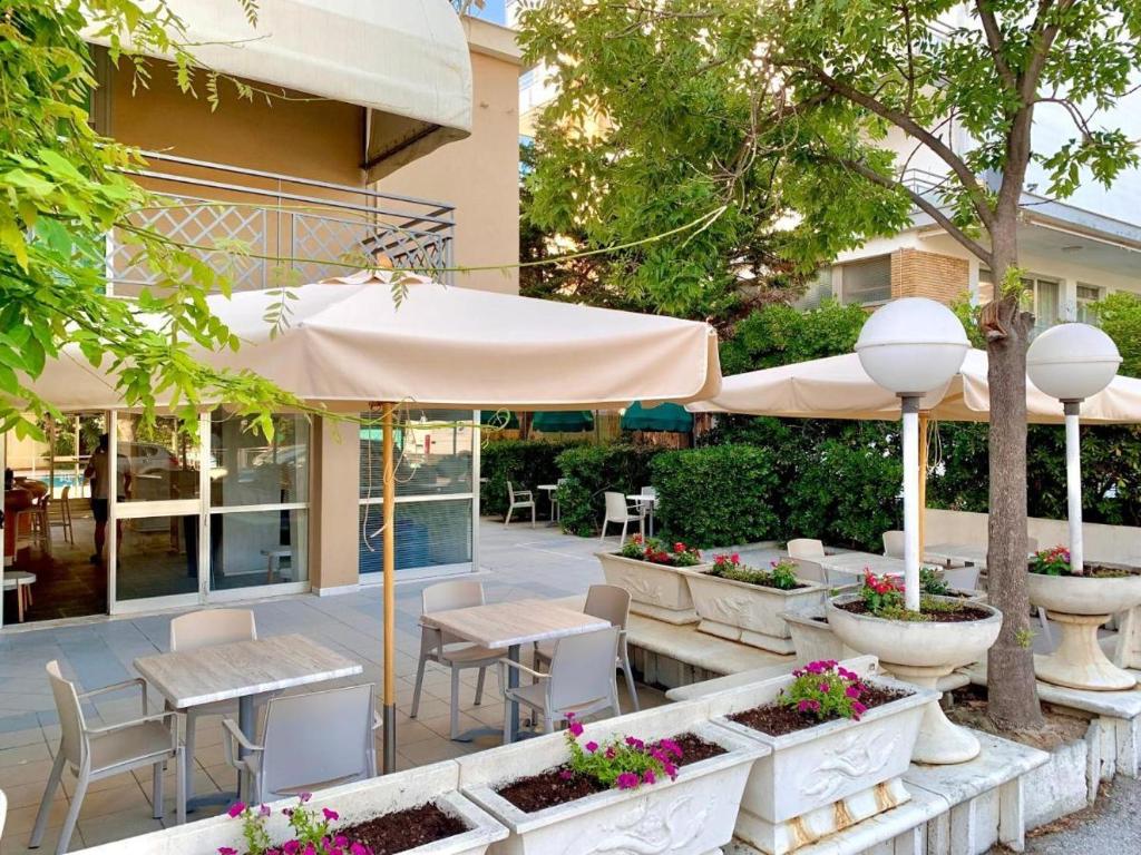un patio avec tables, chaises et un parasol dans l'établissement Hotel Bruna, à Cesenatico