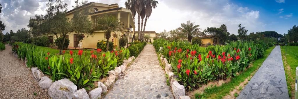 un jardin avec des fleurs rouges en face d'une maison dans l'établissement Horse Country Resort Congress & Spa - Hotel Castello, à Arborea