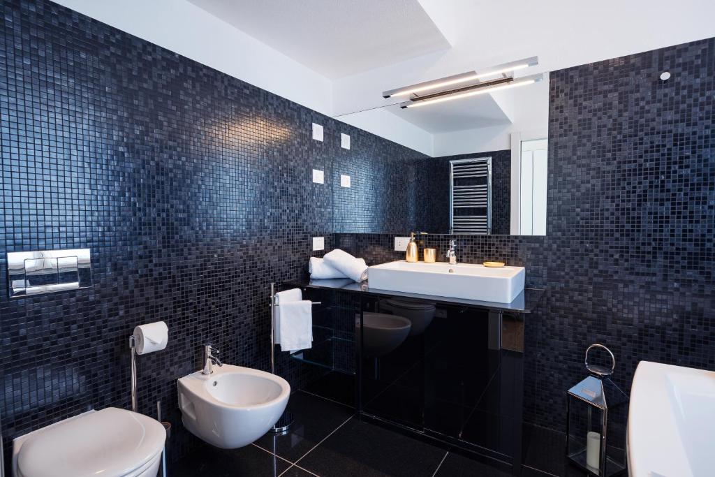 La salle de bains est pourvue de carrelage noir, d'un lavabo et de toilettes. dans l'établissement Villa Meraviglia, à Griante Cadenabbia