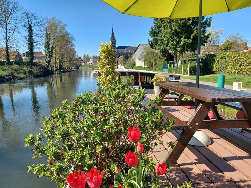 - une table de pique-nique à côté d'une rivière avec des fleurs rouges dans l'établissement Sur la Somme à bord de la péniche Arche de Noé, à Pont-Rémy