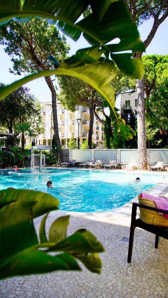 une grande piscine avec de l'eau bleue et des arbres dans l'établissement Hotel Alexander, à Milano Marittima