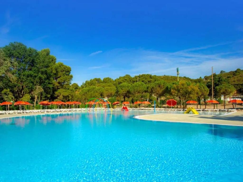 une grande piscine avec des parasols rouges dans un parc dans l'établissement Mobilhome Clim Télé La Falaise 4 étoiles, à Narbonne