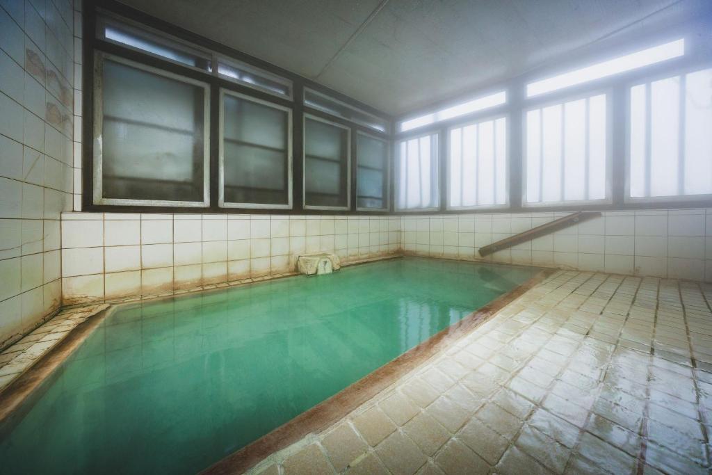 une piscine avec de l'eau verte dans une pièce avec des fenêtres dans l'établissement Yoshidaya, à Zao Onsen