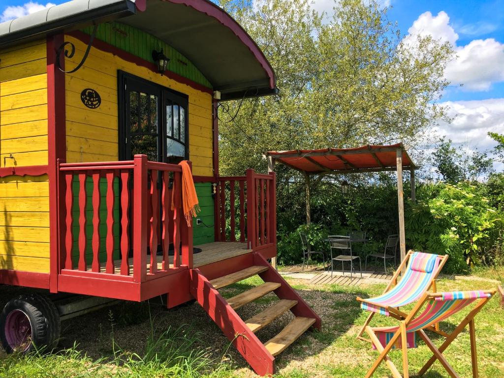 une petite maison jaune et rouge avec une terrasse couverte et 2 chaises dans l'établissement La Dorépontaise ROULOTTE, à Pondaurat