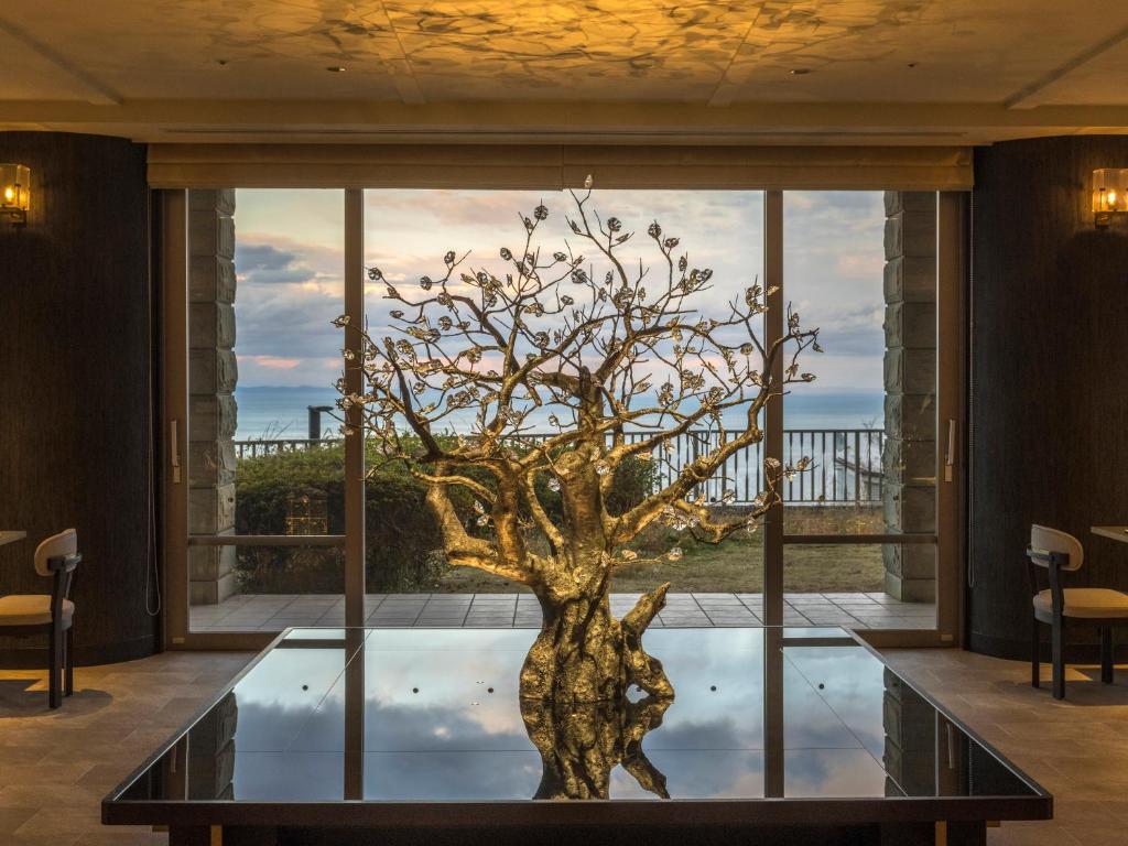 un arbre en bronze sur une table en verre devant une fenêtre dans l'établissement KAMENOI HOTEL Atami, à Atami