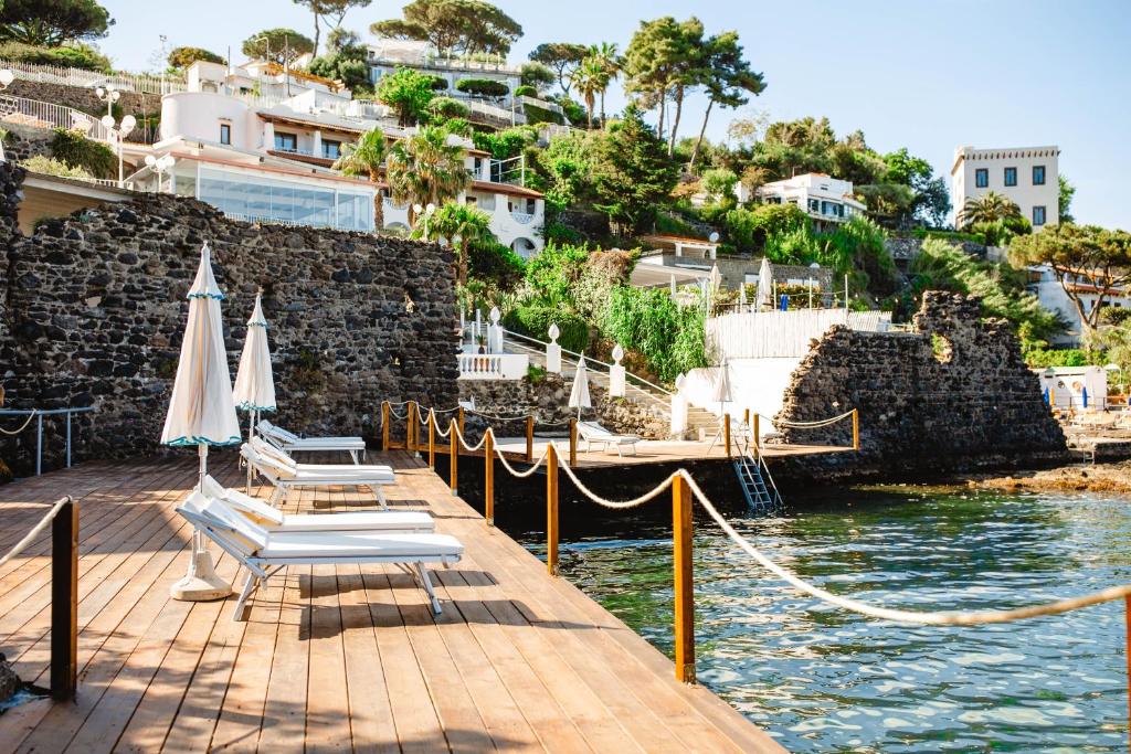 un quai avec des chaises et des parasols sur l'eau dans l'établissement Strand Hotel Delfini, à Ischia