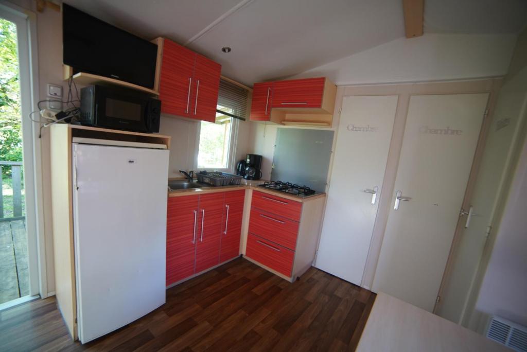 une cuisine avec des armoires rouges et un réfrigérateur blanc dans l'établissement Mobil-home Saint-Chéron 91530 Camping Parc des roches, à Mirgaudon