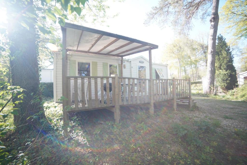 une petite maison avec un chien assis sur un porche dans l'établissement Mobil-home Saint-Chéron 91530 Camping Parc des roches, à Mirgaudon