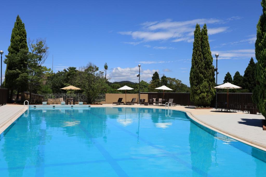 une grande piscine bleue avec des arbres et des parasols dans l'établissement Ginsuisou Choraku, à Kobe