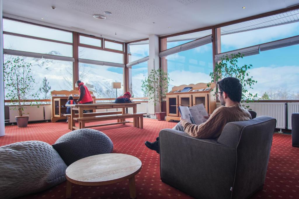 un homme assis dans une chaise dans une pièce avec fenêtres dans l'établissement Belambra Clubs Les Menuires - Neige Et Ciel, aux Menuires 34 autres photos