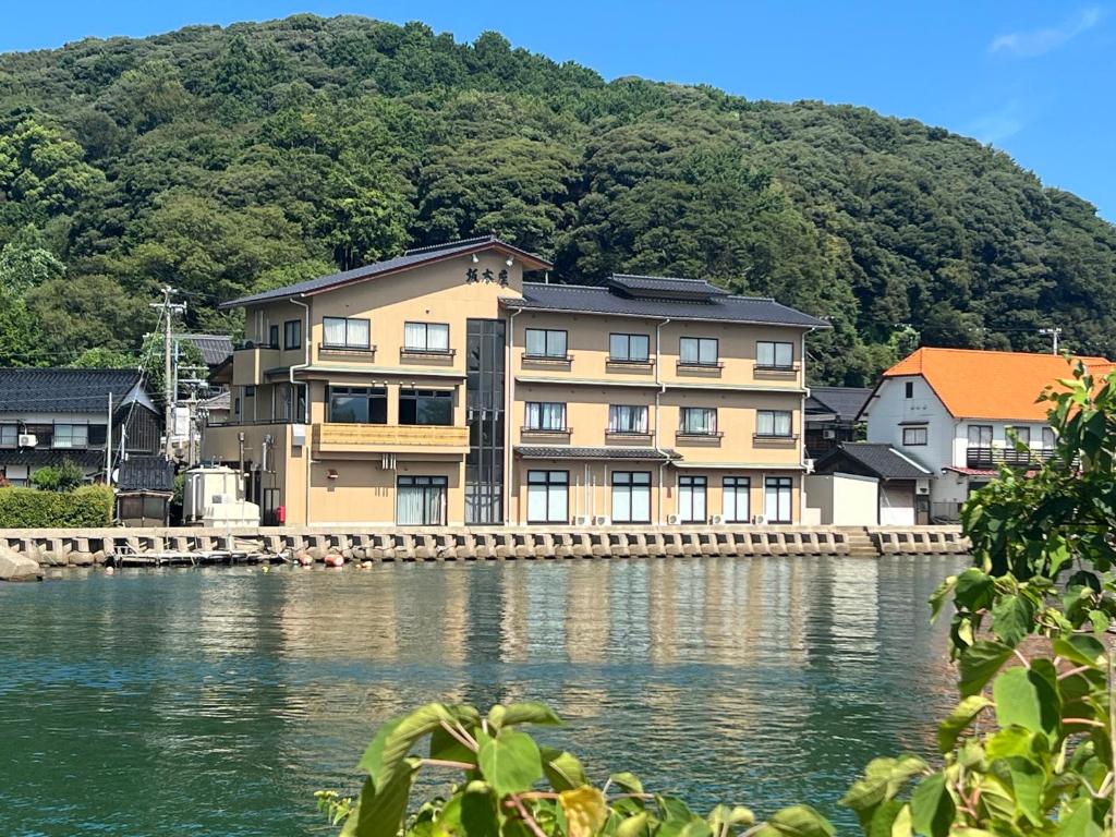 un grand bâtiment sur l'eau à côté d'une montagne dans l'établissement 坂本屋旅館, à Kyōtango