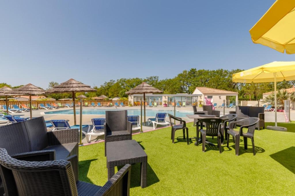 un patio avec tables et chaises et une piscine dans l'établissement Camping maeva Escapades Le Bois Joli, à Bois-de-Cené
