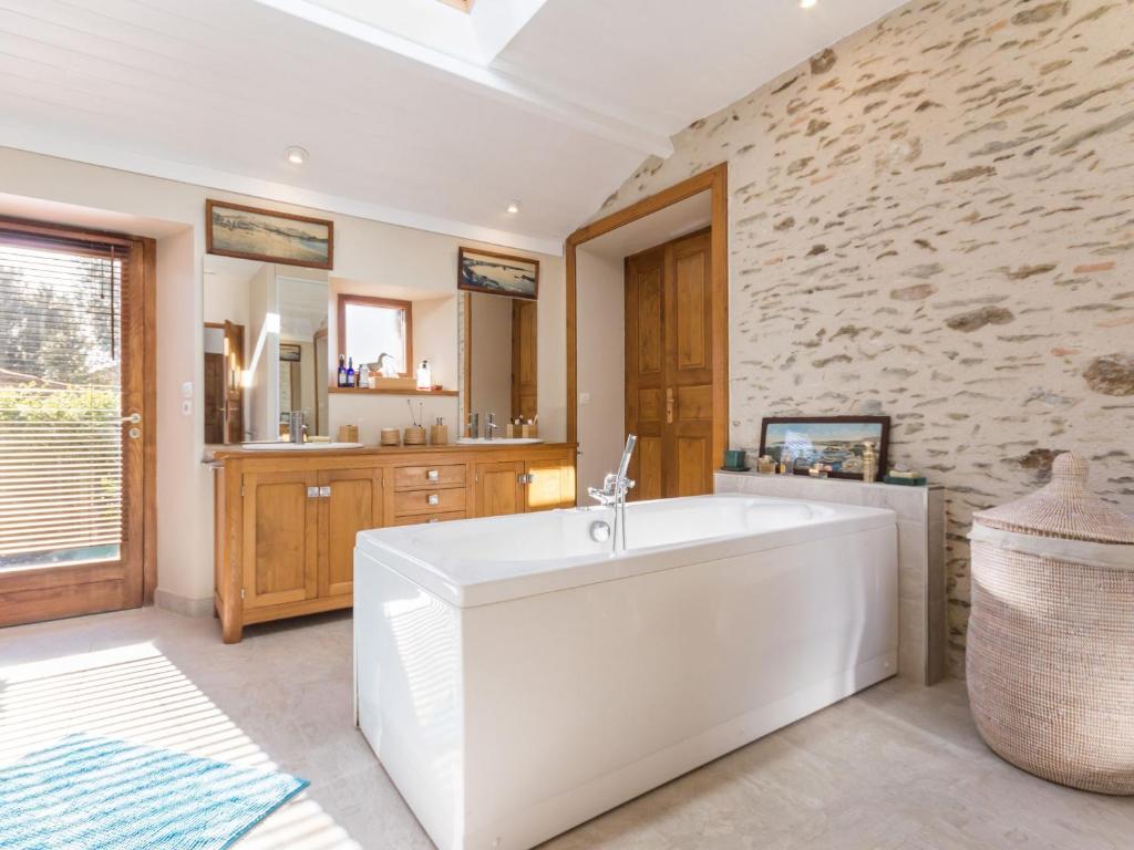La salle de bains est pourvue d'une baignoire blanche et d'un mur en pierre. dans l'établissement Gîte familial spacieux avec piscine naturelle, proche Nantes - FR-1-306-1218, à La Limouzinière