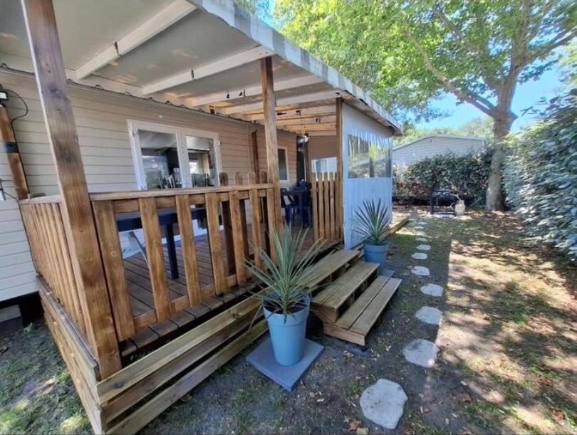 une maison avec une terrasse couverte en bois et deux plantes en pot dans l'établissement Mobil-home Camping Siblu La Reserve ****, à Gastes