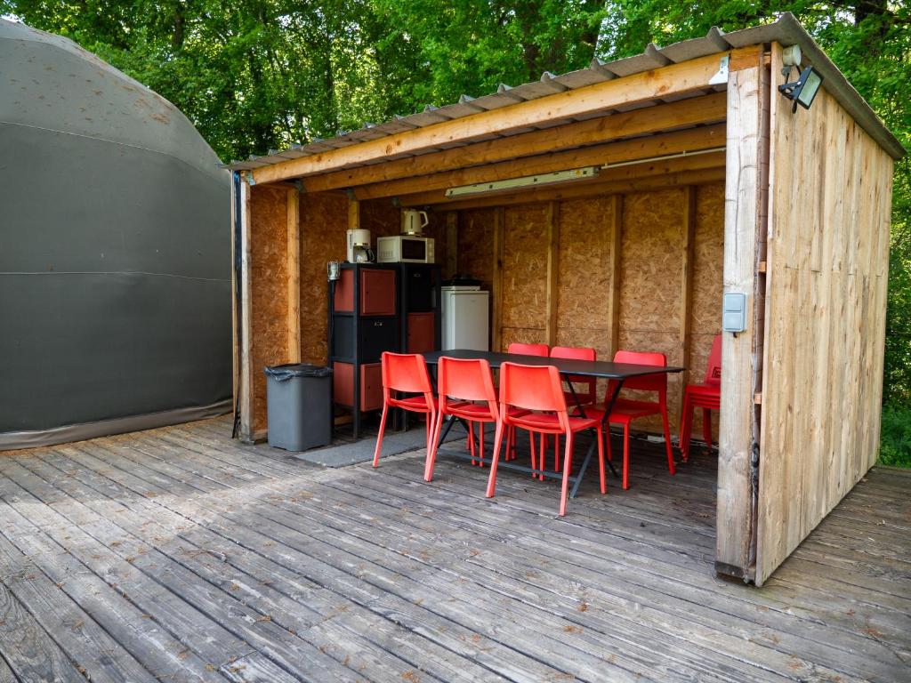une terrasse en bois avec une table et des chaises rouges dans l'établissement Évasion nature, dômes & lac privé près Bordeaux, à Sadirac