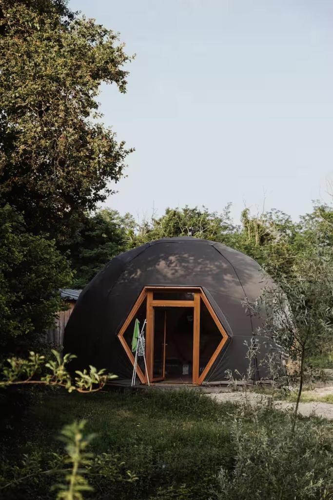 une maison en dôme noir avec une porte dans une cour dans l'établissement Évasion nature, dômes & lac privé près Bordeaux, à Sadirac