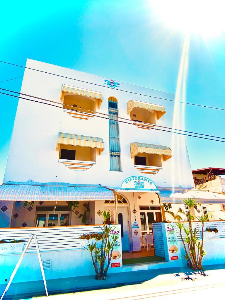 un bâtiment blanc avec des fenêtres jaunes sur une rue dans l'établissement Albergo 2 Mari, à Leuca