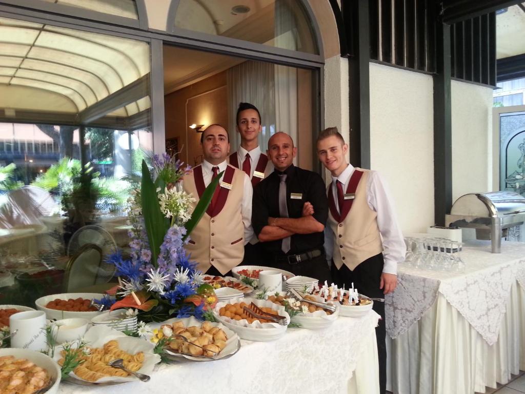un groupe d'hommes debout devant une table avec de la nourriture dans l'établissement Amsterdam Suite Hotel & SPA, à Rimini