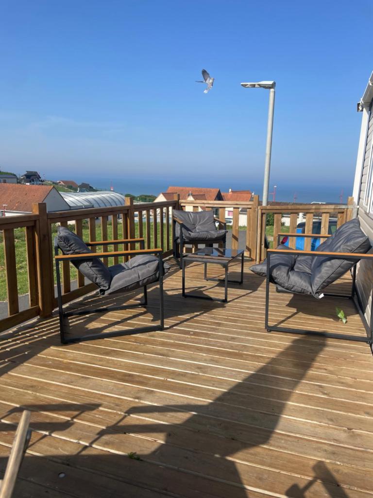 trois chaises sur une terrasse avec l'océan en arrière-plan dans l'établissement Mobil home au bord de la mer, vue sur la mer camping de la falaise à Equihen-Plage, à Équihen-Plage