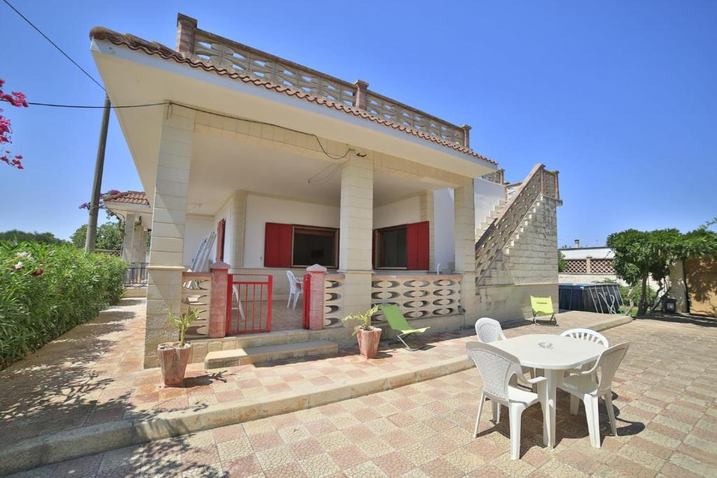 une petite maison blanche avec une table et des chaises dans l'établissement Villetta Giusy con piscina a soli 700 mt dalla spiaggia di San Pietro in Bevagna, à San Pietro in Bevagna