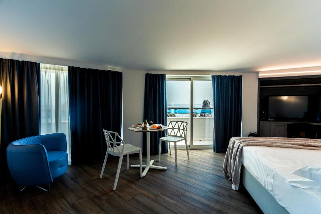 une chambre d'hôtel avec un lit, une table et des chaises dans l'établissement Grand Hotel Faraglioni, à Aci Trezza