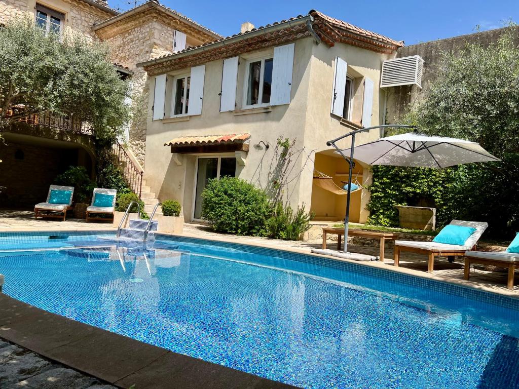 - une piscine avec des chaises et un parasol à côté d'une maison dans l'établissement Gîte familial 6 personnes climatisé, piscine partagée chauffée, proche Nîmes, Uzès, Pont du Gard, Cévennes, à Saint-Géniès-de-Malgoirès
