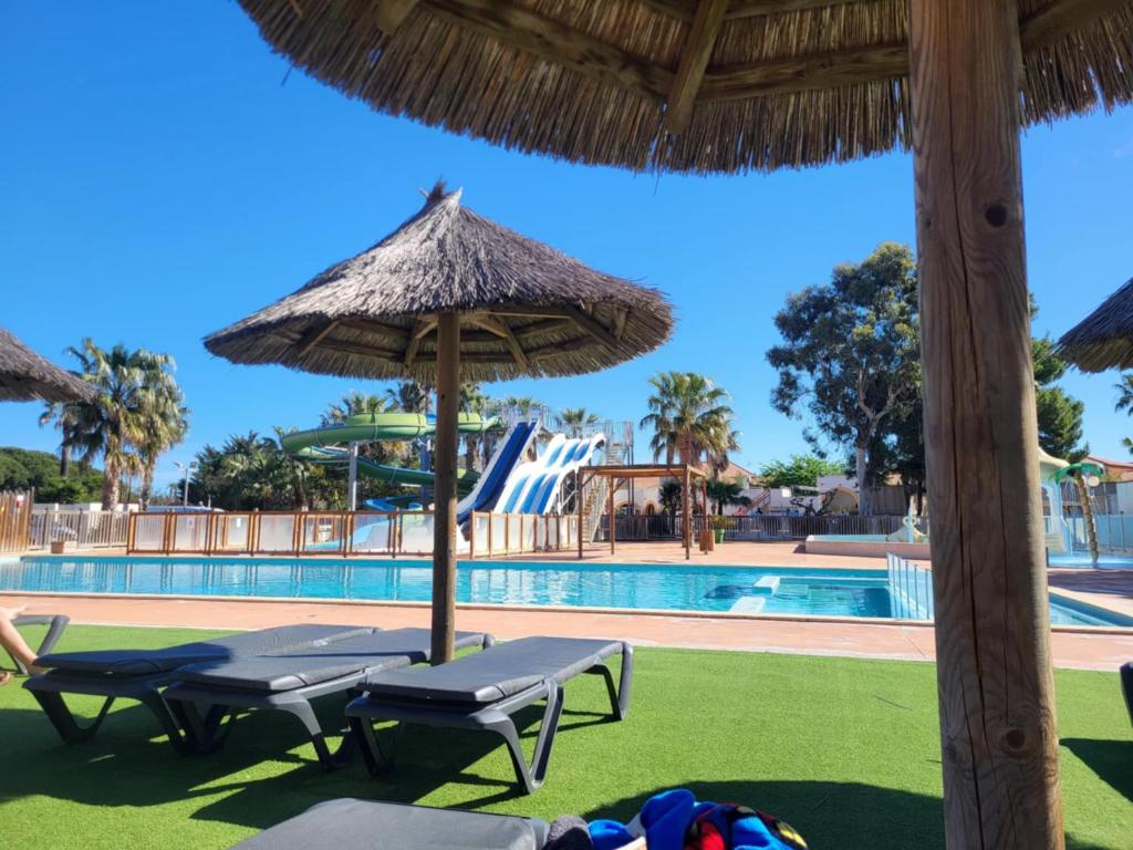 - une piscine avec des chaises, un parasol et un toboggan dans l'établissement La palmeraie à torreilles, à Torreilles