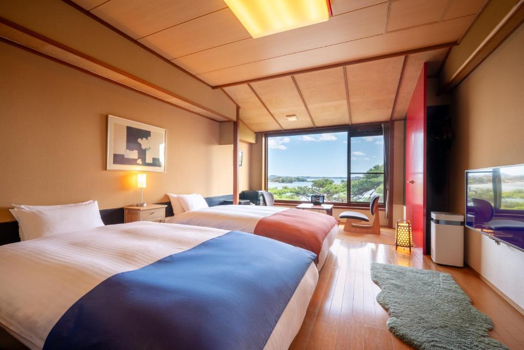 deux lits dans une chambre avec une grande fenêtre dans l'établissement Komatsu-kan Kofu-tei, à Matsushima