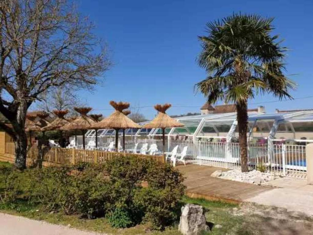 un complexe avec des parasols en paille, des chaises et des arbres dans l'établissement Camping 4 étoiles - Piscine - eed0fe, à Thégra