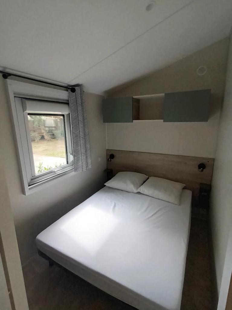 une petite chambre avec un lit blanc et une fenêtre dans l'établissement Mobil home prémium 8 pers camping 4 étoiles, à Saint-Cyprien 22 autres photos