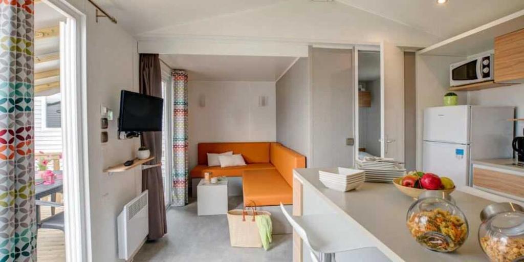 un salon avec un canapé orange et une cuisine dans l'établissement Camping 5 étoiles - Parc aquatique - eeiaid, à Pénestin