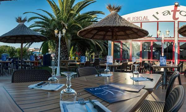 une table en bois avec des chaises et des parasols dans un restaurant dans l'établissement Mobil-Home VO42 Camping La Carabasse VIAS-Plage, à Vias